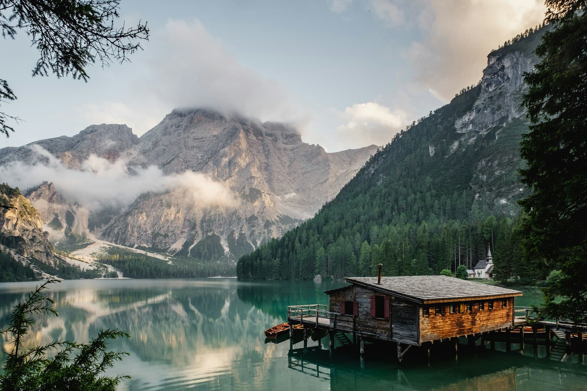 A boathouse on a still mountain lake ringed by pines, under low cloud